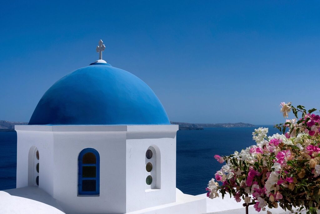 Λευκό εκκλησάκι με γαλάζιο τρούλο πάνω από το Αιγαίο